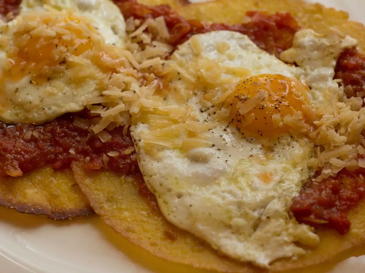 Huevos fritos sobre tortitas de maíz con salsa de tomate y queso rallado por encima
