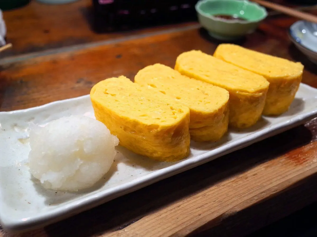 Rodajas de tortilla japonesa enrollada tamagoyaki con un montículo de arroz blanco en un plato alargado