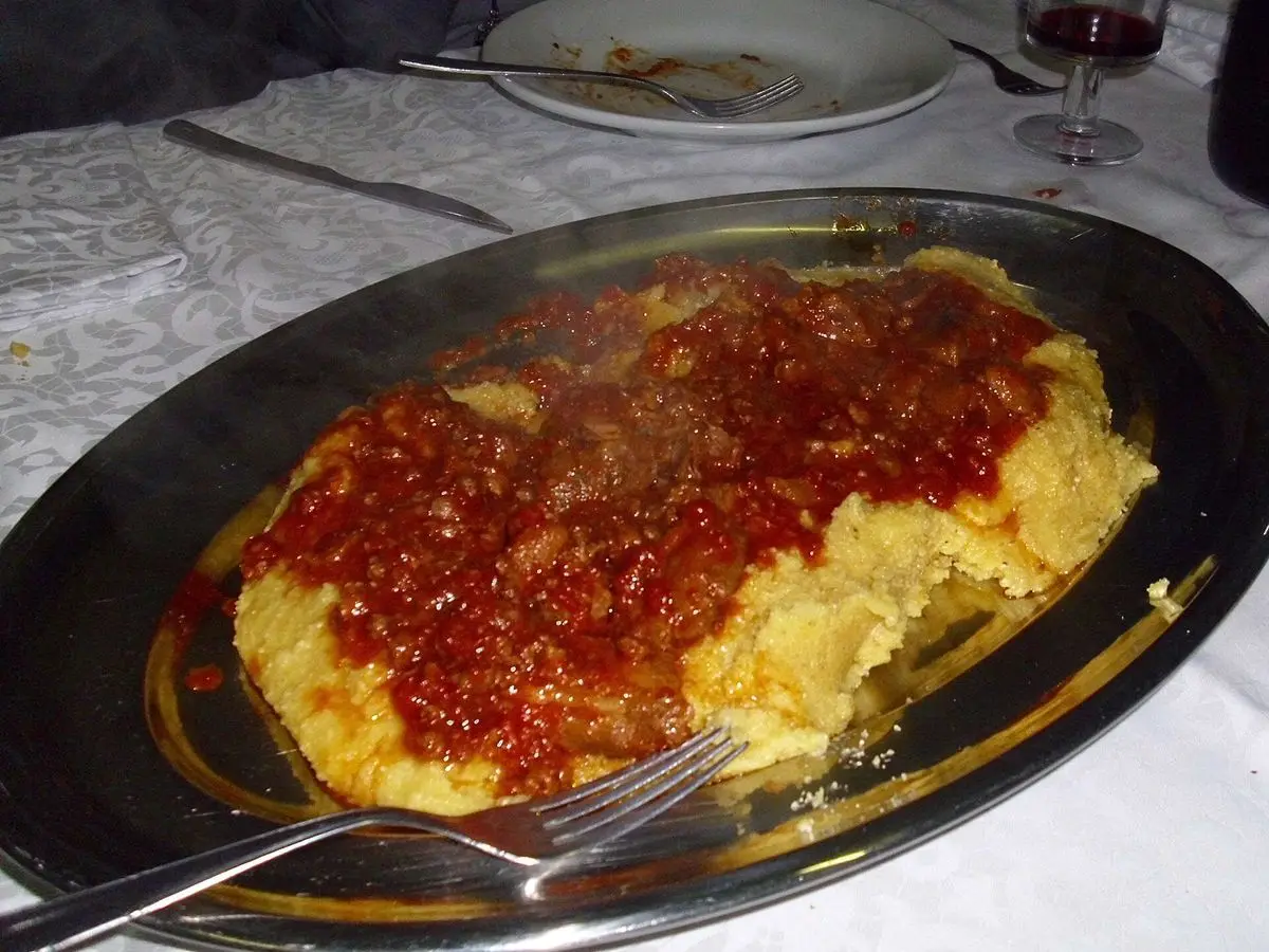 Fuente oscura con polenta de maíz cremosa cubierta de un guiso de carne en salsa de tomate