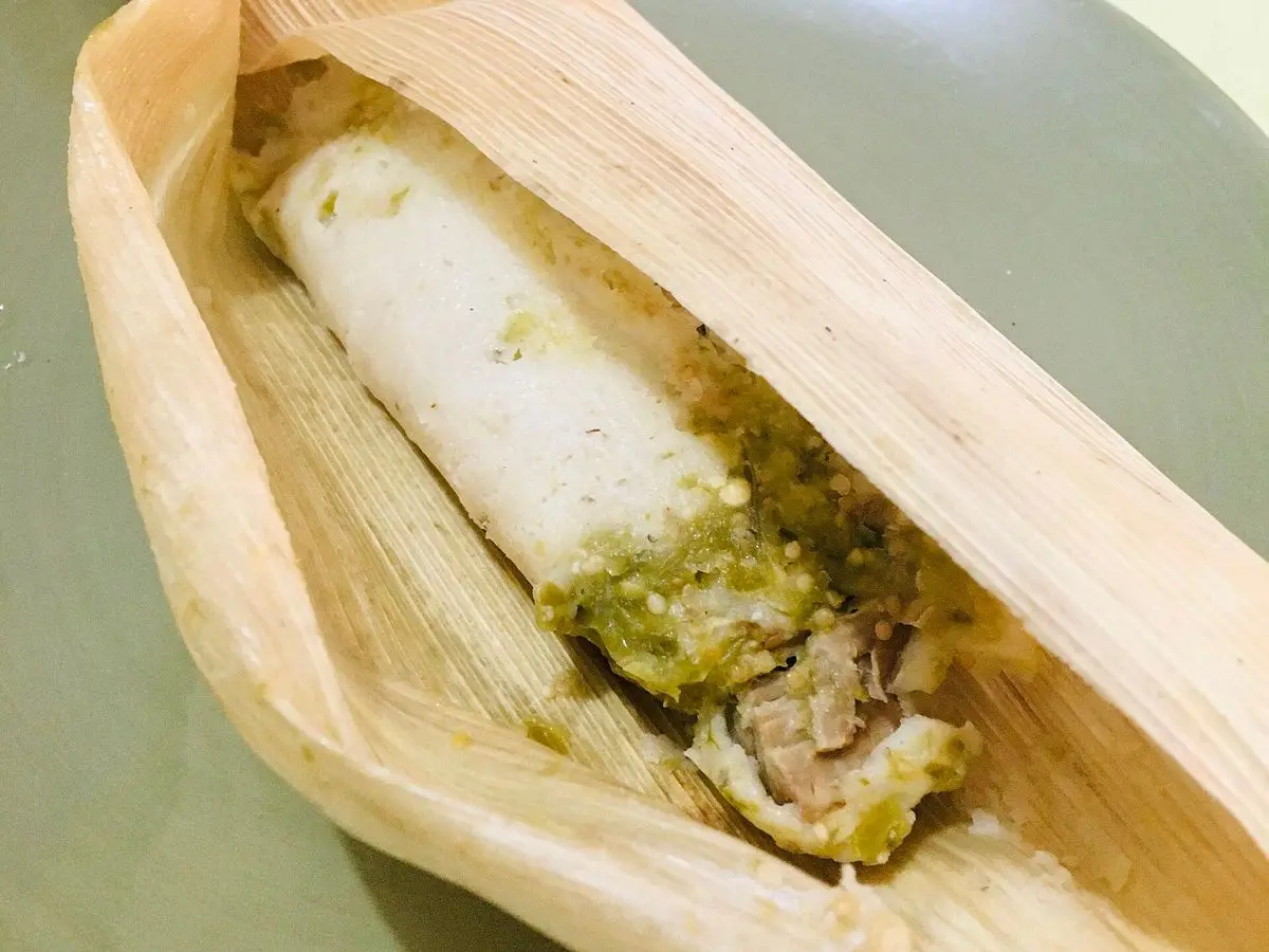Tamal abierto en su hoja de maíz mostrando masa blanca rellena de carne en salsa verde