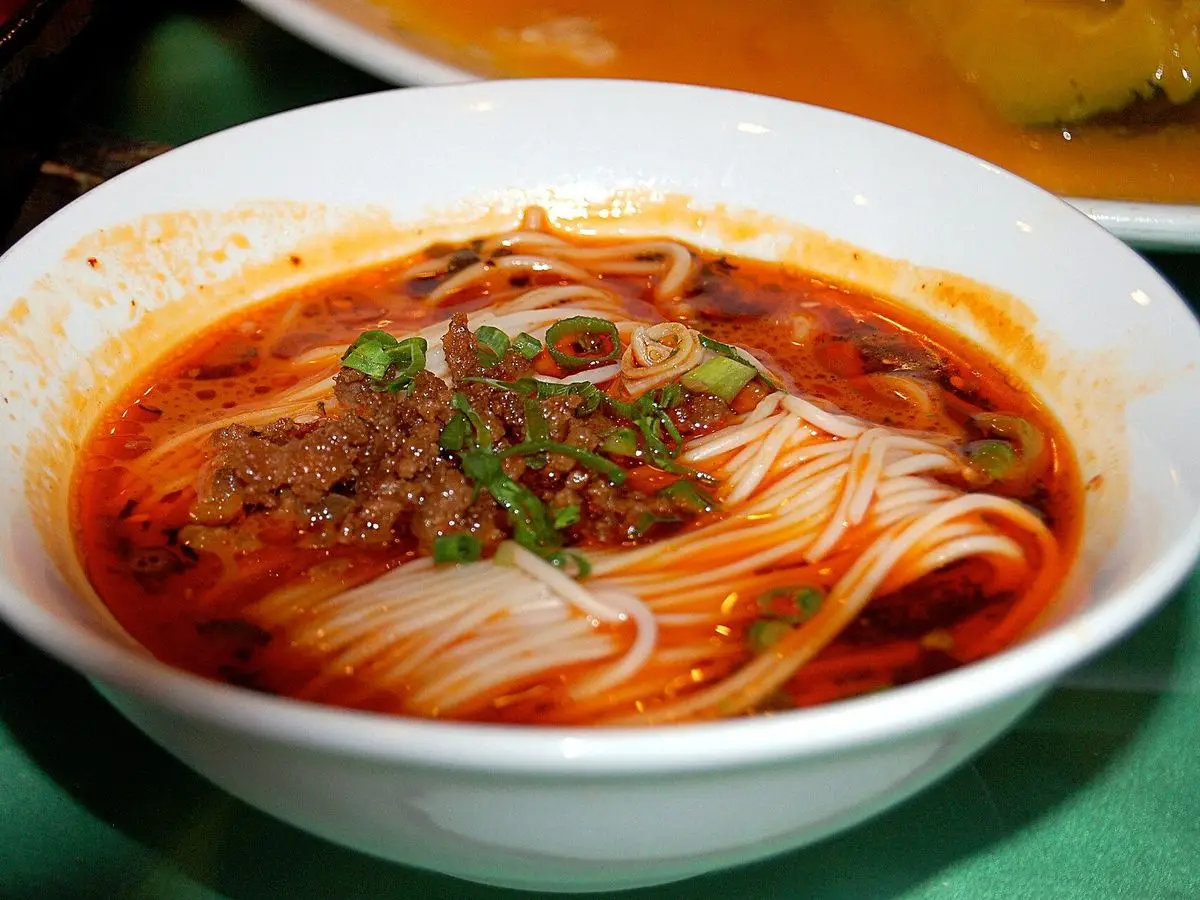 Cuenco blanco de fideos en caldo rojo picante con picadillo dorado y cebolleta por encima