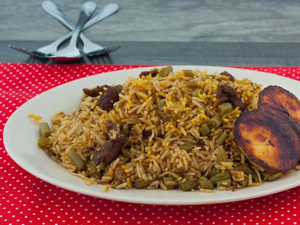 Plato con arroz con judías verdes, trozos de carne y plátano frito sobre mantel rojo