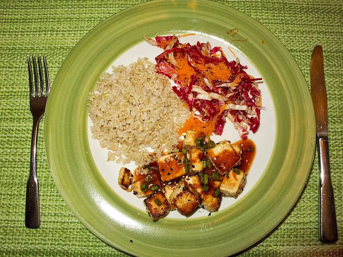 Plato con tofu en dados, arroz integral y ensalada de lombarda y zanahoria sobre un mantel verde