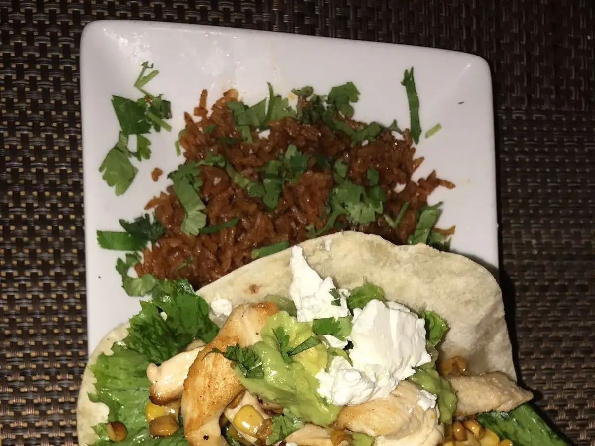 Dos tacos de pollo con aguacate, lechuga, maíz y queso fresco sobre una bandeja