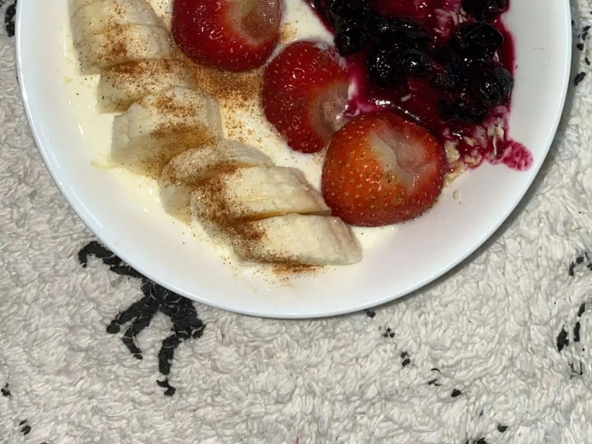 Plato con plátano en rodajas, fresas enteras y compota oscura de frutos rojos sobre un fondo blanco