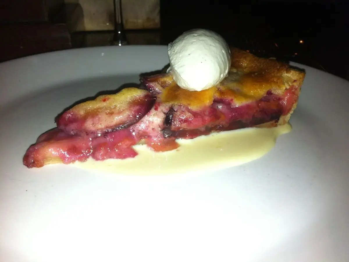 Porción de tarta fina de ciruelas rojas con una bola de helado sobre un plato blanco