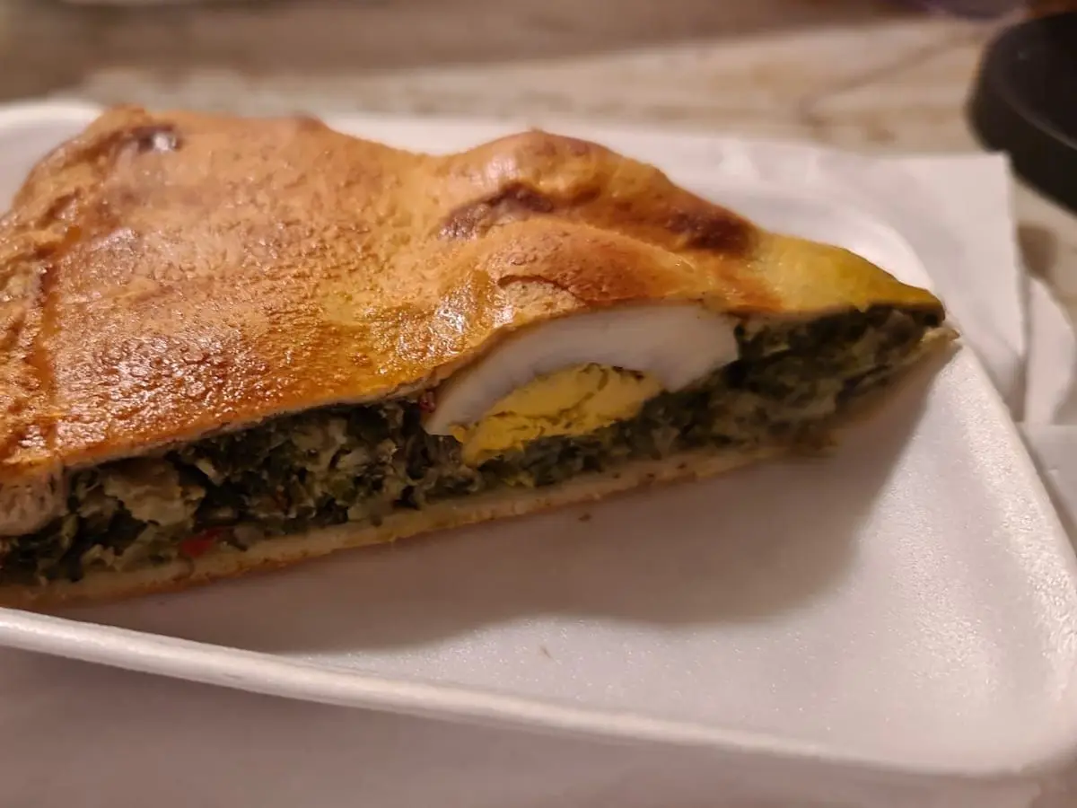 Porción de tarta pascualina con relleno de verdura verde y mitad de huevo duro en un plato blanco
