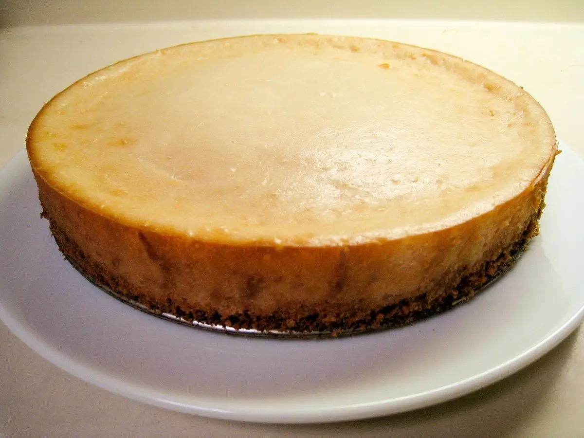 Tarta de queso vegana entera de color claro sobre base de galleta y un plato blanco