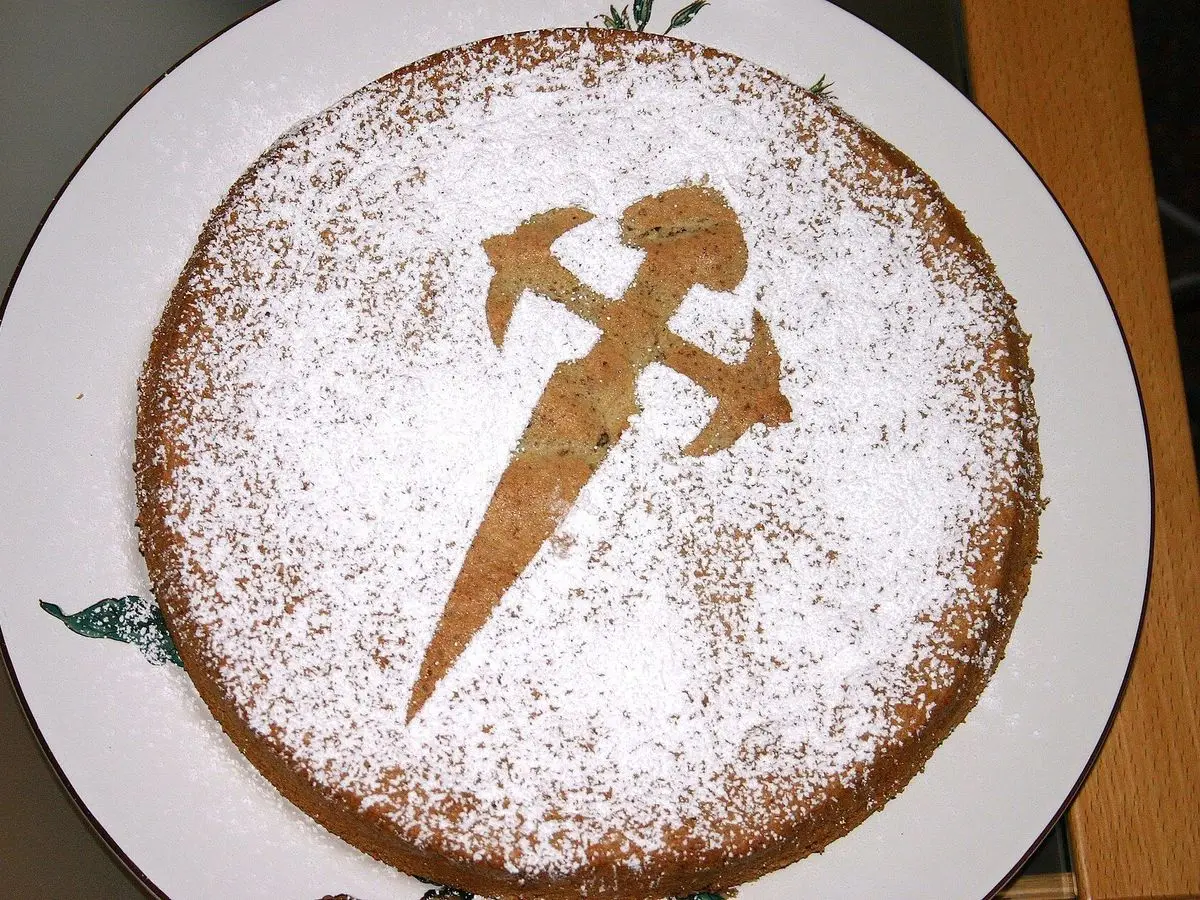 Tarta de Santiago espolvoreada de azúcar glas con la cruz de la espada marcada en un plato