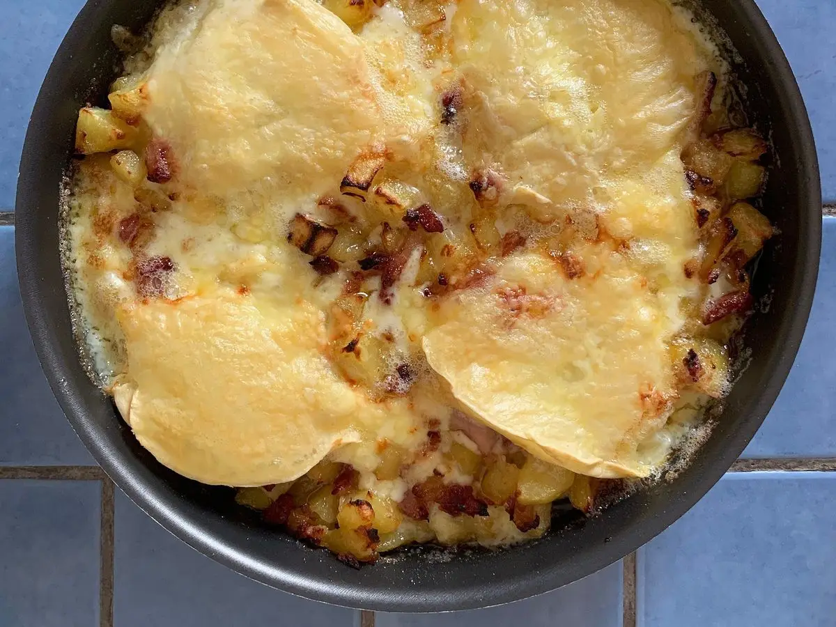 Tartiflette recién salida del horno con queso gratinado, patata y cebolla en una fuente oscura