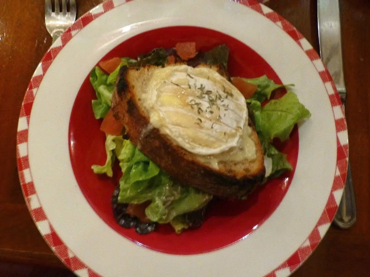 Tostada de pan rústico con queso de cabra gratinado sobre ensalada verde en un plato rojo
