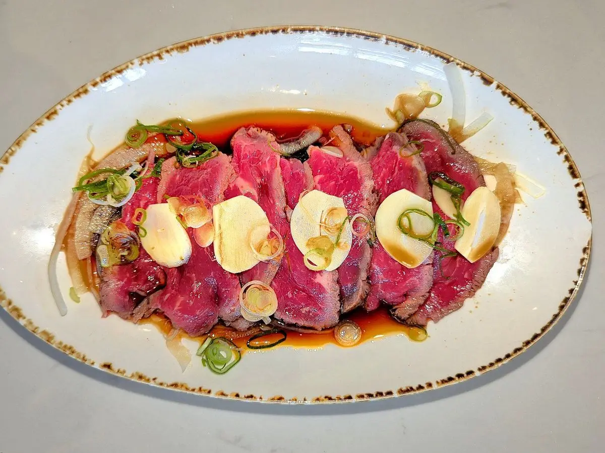 Láminas de tataki de ternera poco hecha con ajo laminado y cebolleta en un plato ovalado