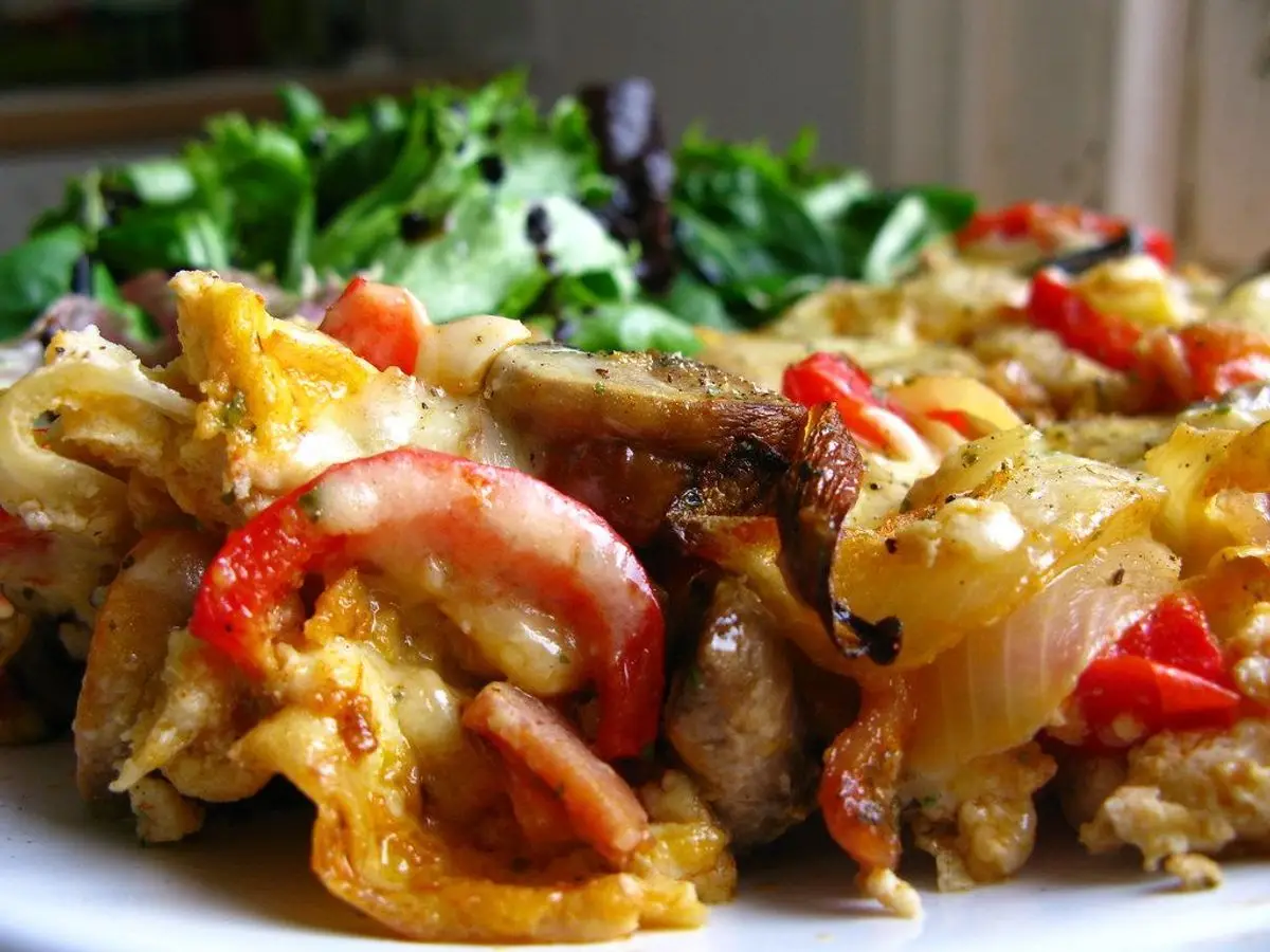 Tortilla de huevo rellena de pimiento, tomate, cebolla y trozos de carne sobre un plato, con hojas verdes al fondo