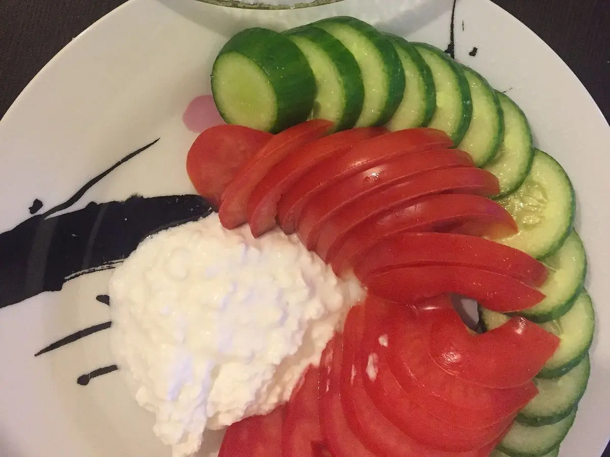 Plato blanco con rodajas de pepino y tomate, una base de queso fresco blanco y aguacate machacado