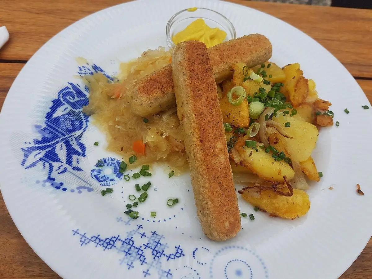 Plato decorado con salchichas vegetales doradas, chucrut y patatas salteadas con cebollino