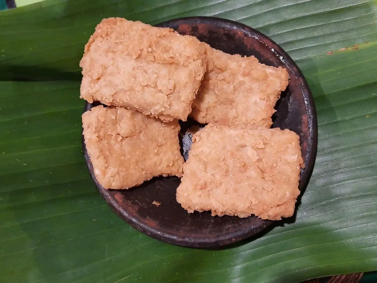 Trozos de tempeh frito y dorado en un cuenco de madera sobre una hoja de plátano