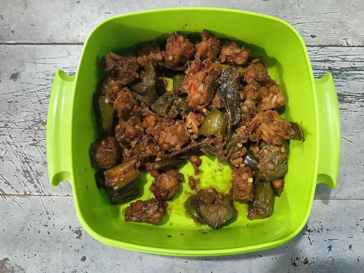 Tempeh salteado en dados con salsa oscura en un recipiente verde sobre una mesa gris