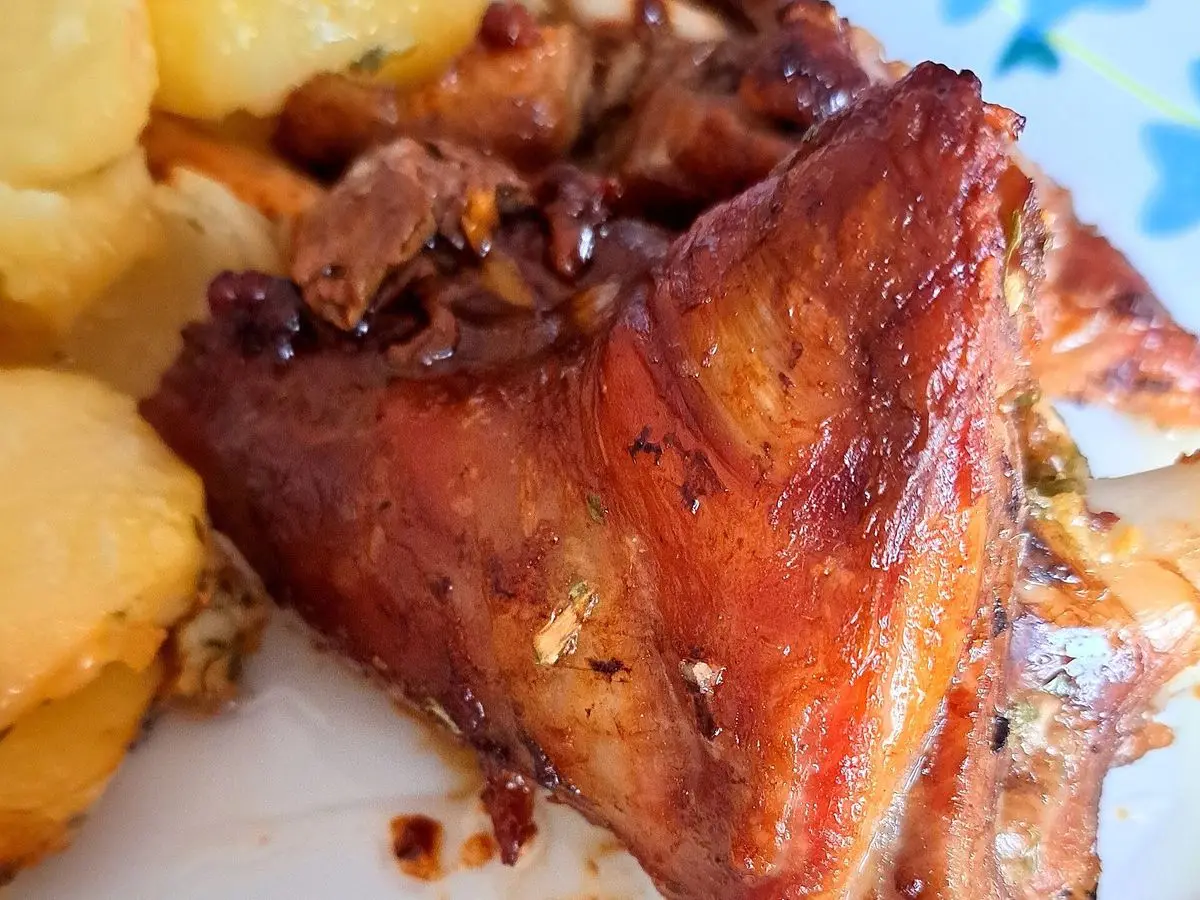 Paletilla de cordero asada y dorada sobre rodajas de patata en un plato