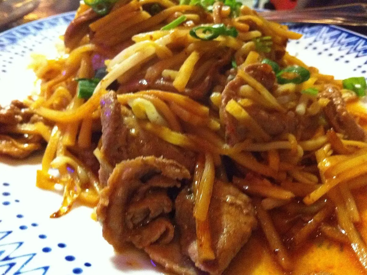 Ternera salteada con tiras de brotes de bambú y cebolleta en salsa oscura sobre un plato decorado