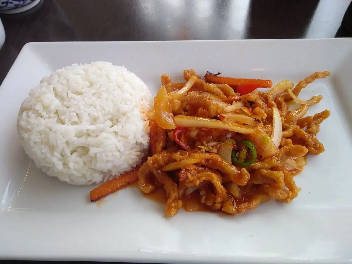 Tiras de ternera crujiente con zanahoria y pimiento en salsa junto a arroz blanco en un plato rectangular