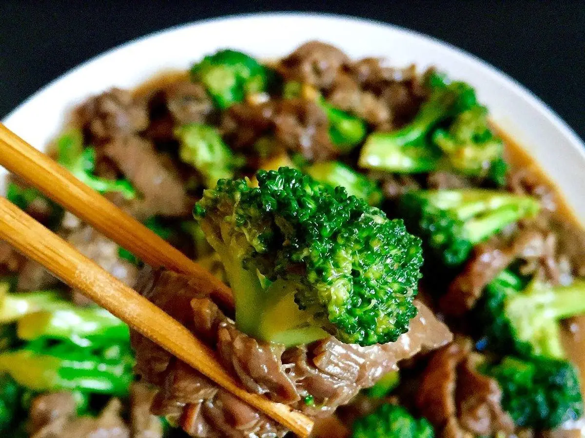 Tiras de ternera salteadas con ramilletes de brócoli verde en un cuenco blanco, con palillos