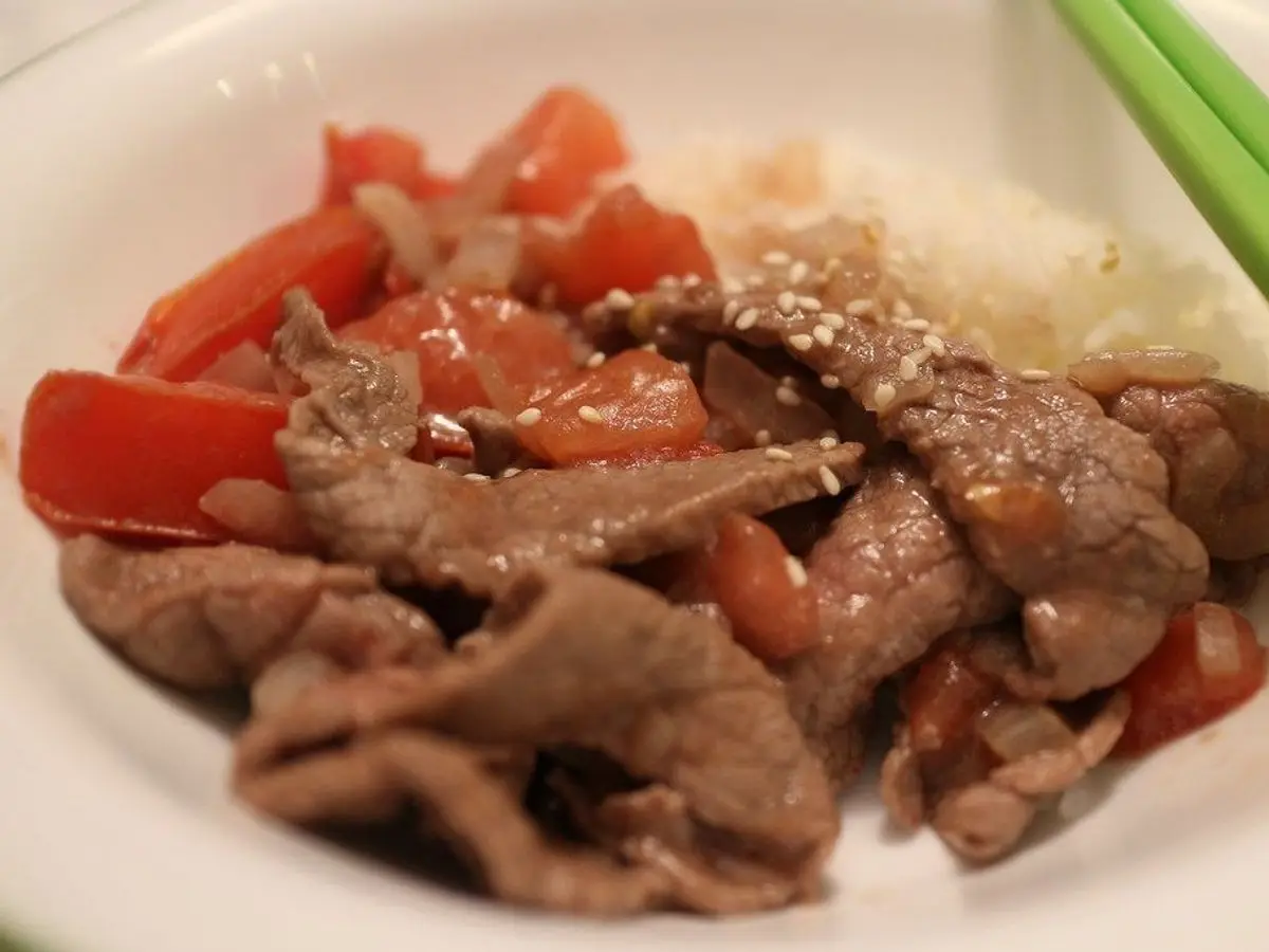 Plato de tiras de ternera salteadas con gajos de tomate sobre arroz blanco, con palillos al lado