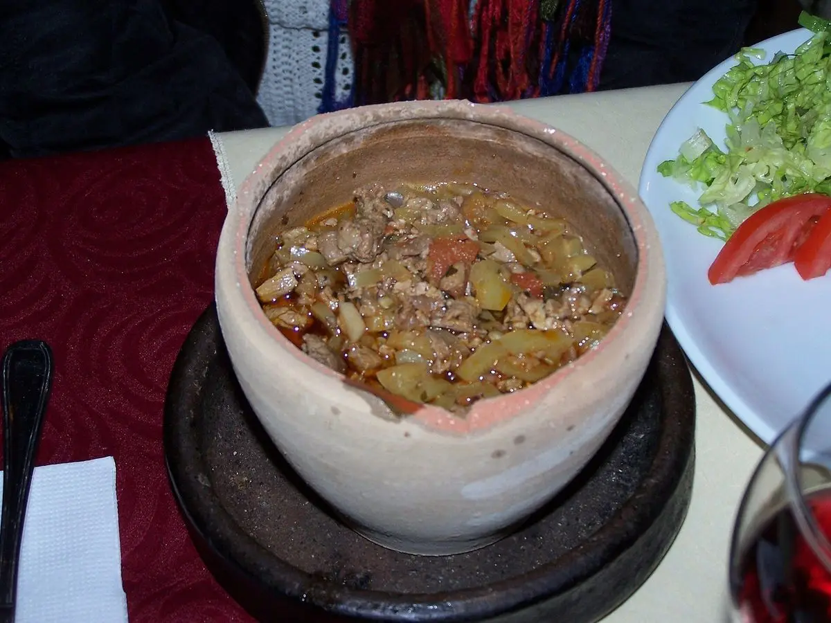 Cazuela de barro con guiso de carne y verduras troceadas servida sobre un soporte de madera
