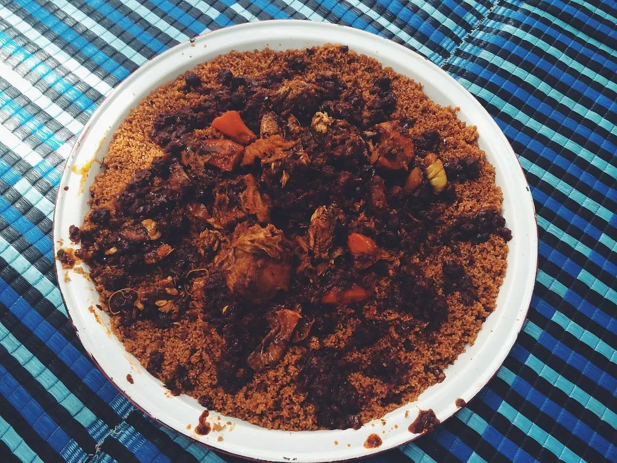 Plato blanco de arroz rojo senegalés con trozos de carne y verdura sobre un mantel azul a rayas