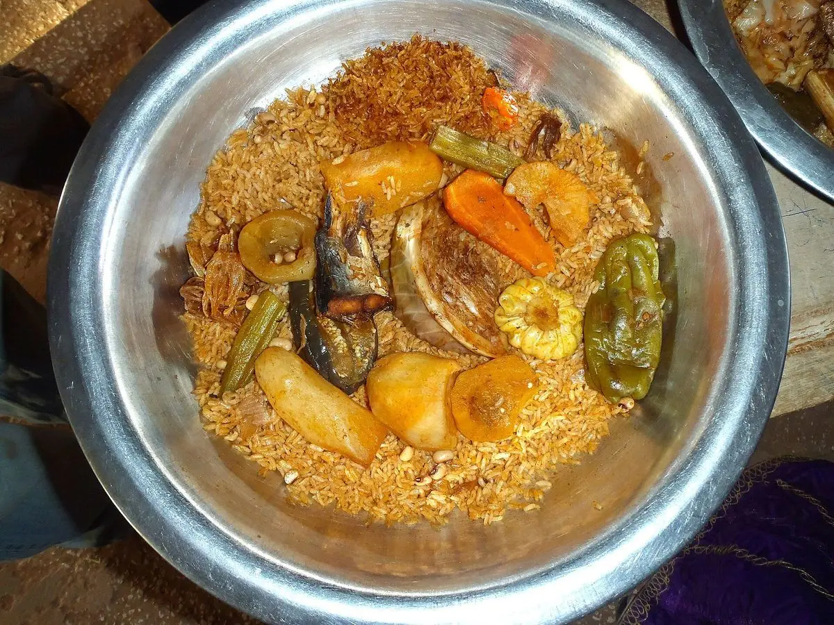 Fuente de metal con arroz thieboudienne con pescado, zanahoria, pimientos y verduras