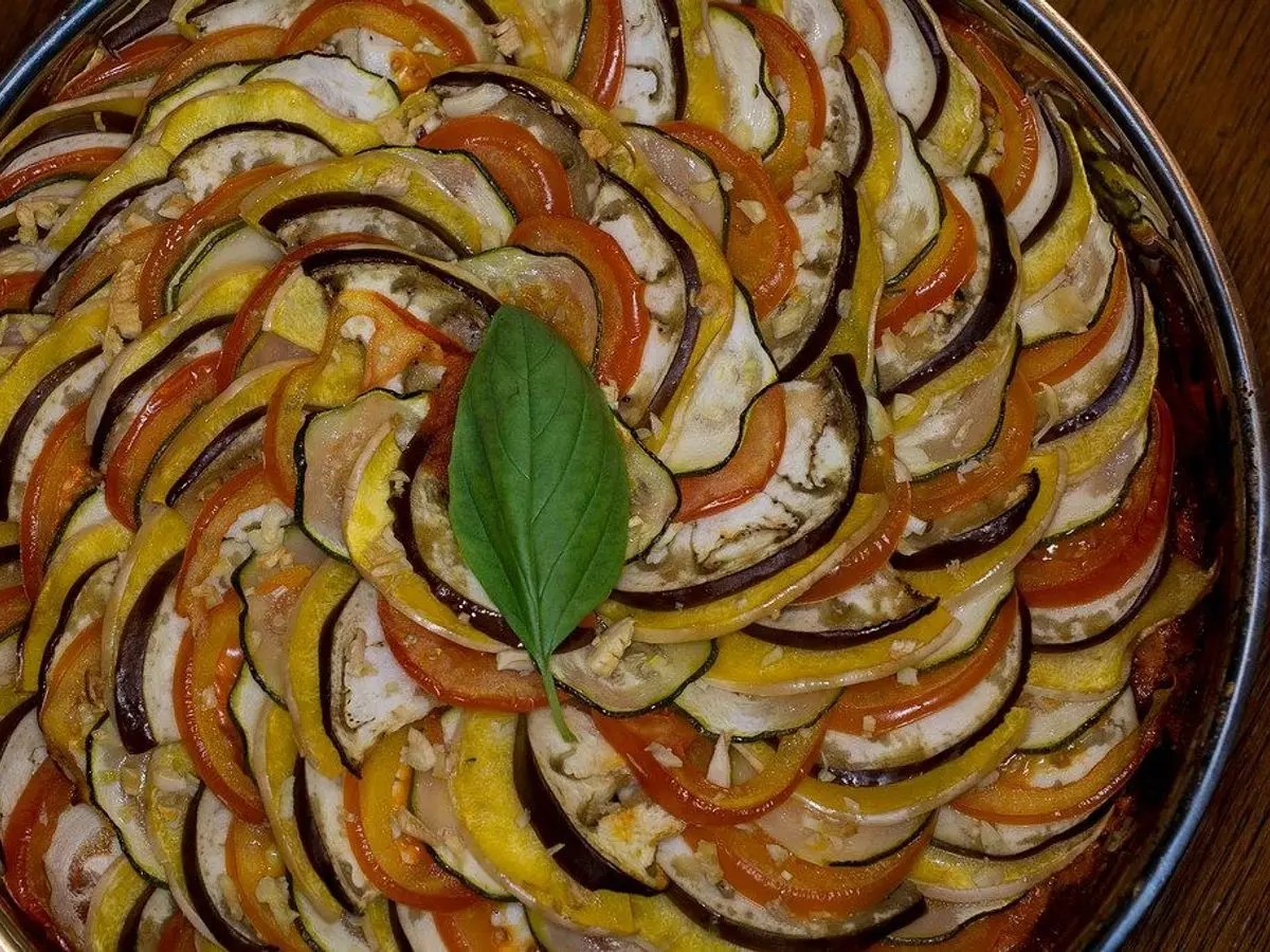 Tian de verduras en espiral con berenjena, calabacín y tomate en rodajas con una hoja de albahaca