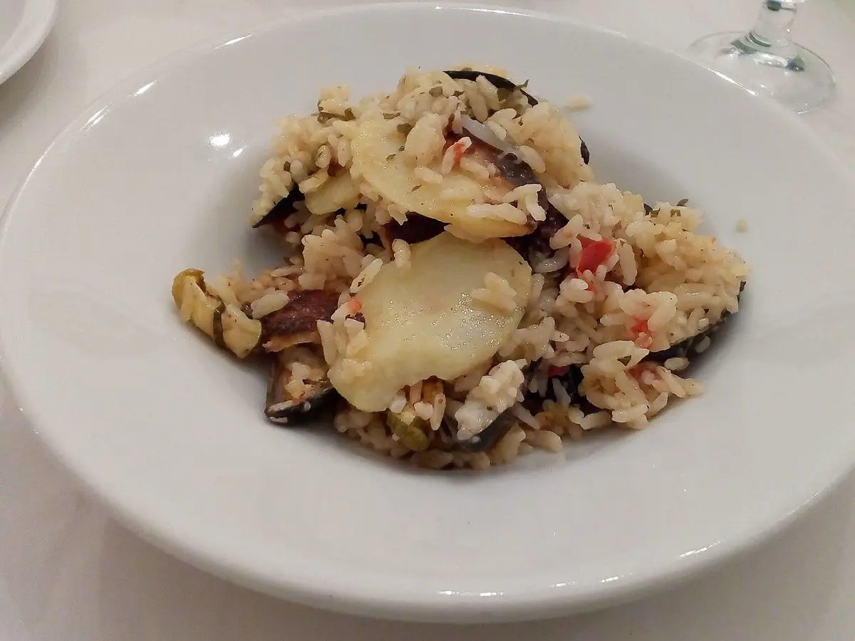 Plato hondo blanco con arroz, patata en rodajas y mejillones gratinados