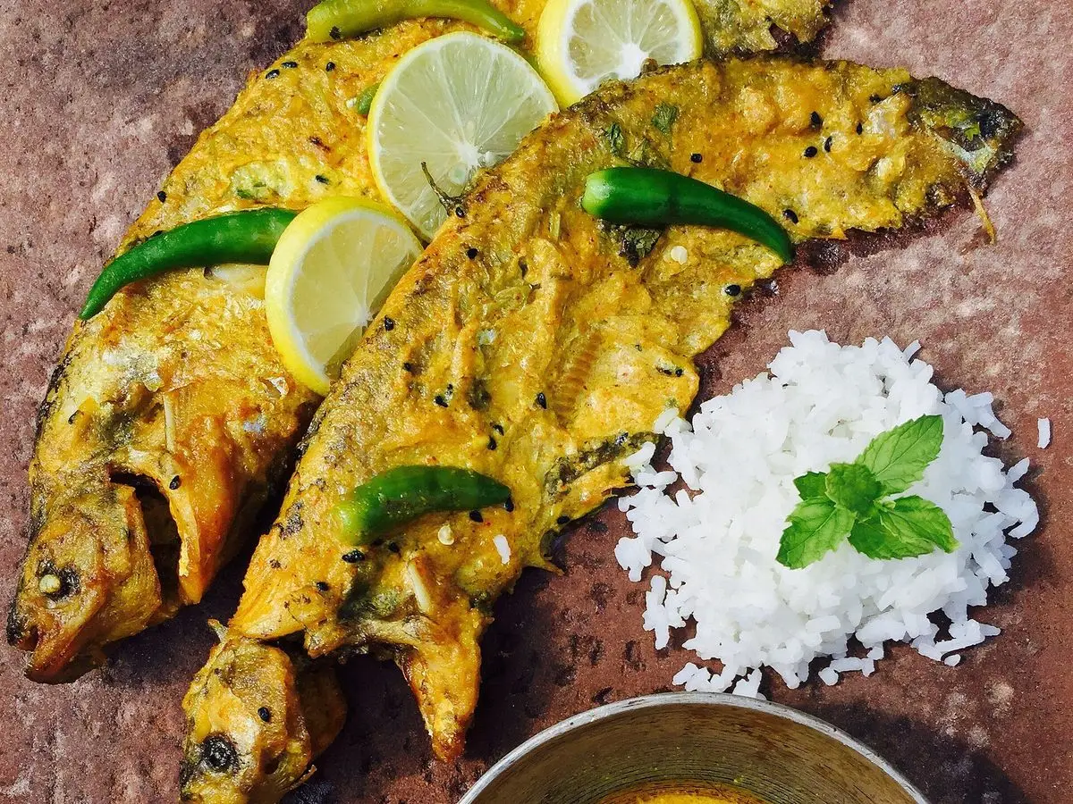 Dos pescados dorados con guindilla verde y rodaja de limón junto a arroz blanco y un cuenco de salsa amarilla