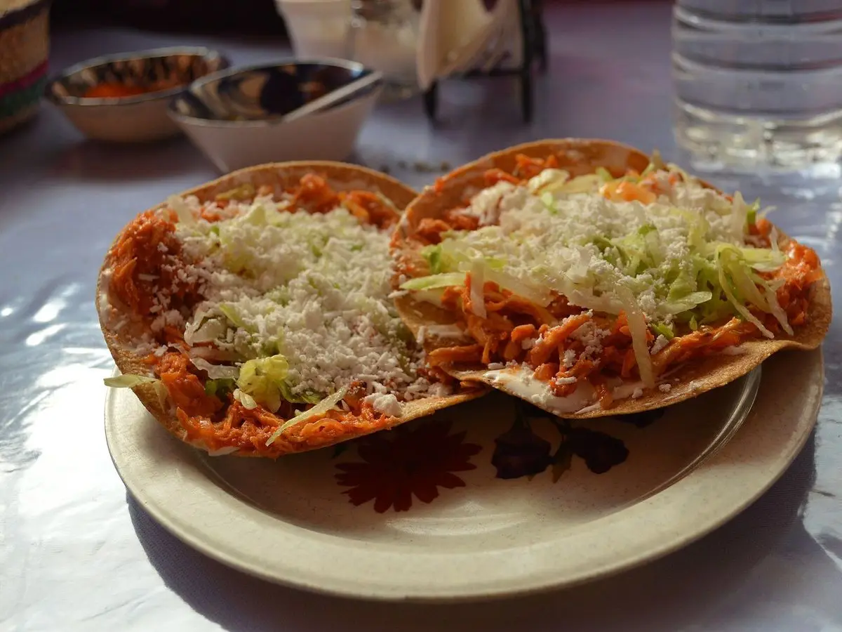 Dos tostadas de tinga con lechuga y queso rallado servidas en un plato