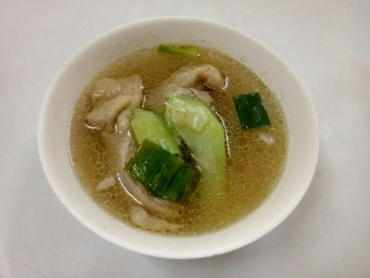 Cuenco blanco de sopa clara de pollo con chayote en rodajas y hojas verdes