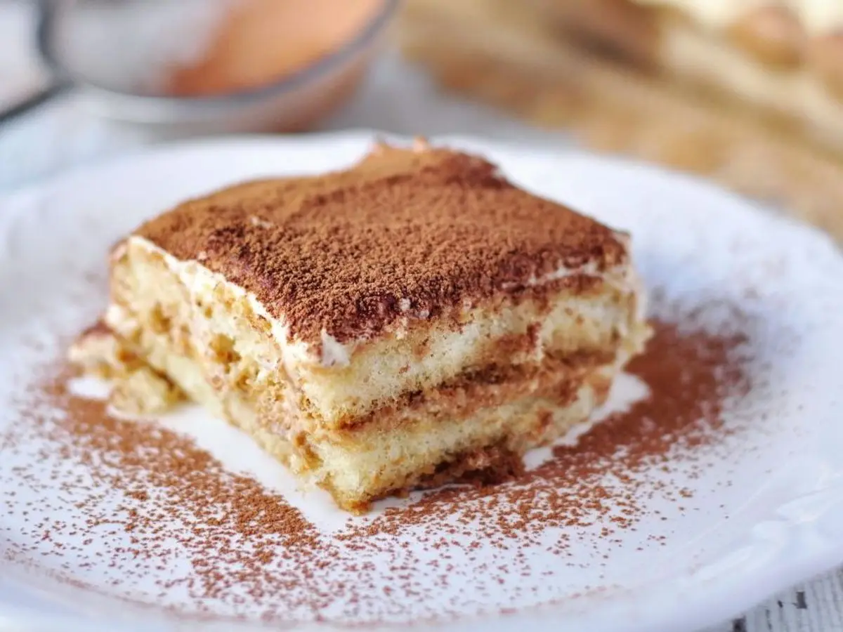 Porción de tiramisú espolvoreada de cacao sobre un plato blanco
