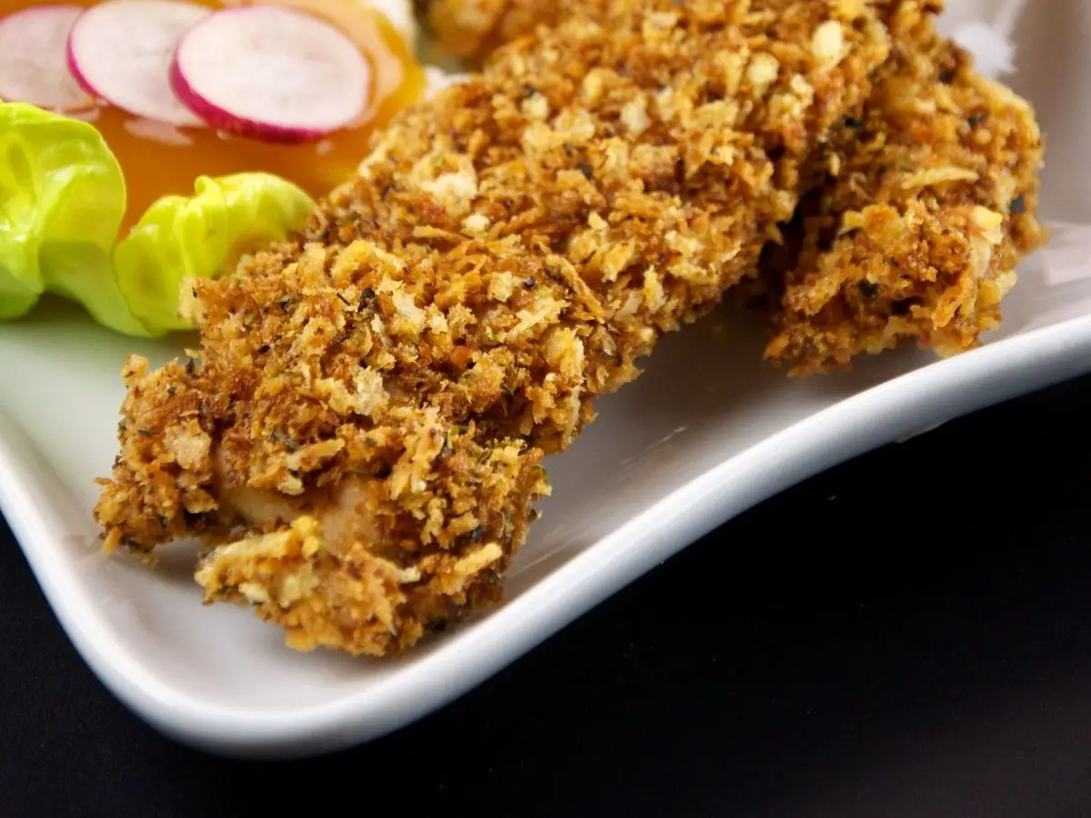 Tiras de pollo crujiente con cobertura dorada junto a lechuga y rábano en un plato