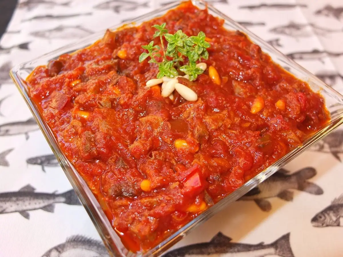 Fuente de cristal con sofrito de tomate y pimiento con atún, piñones y perejil por encima