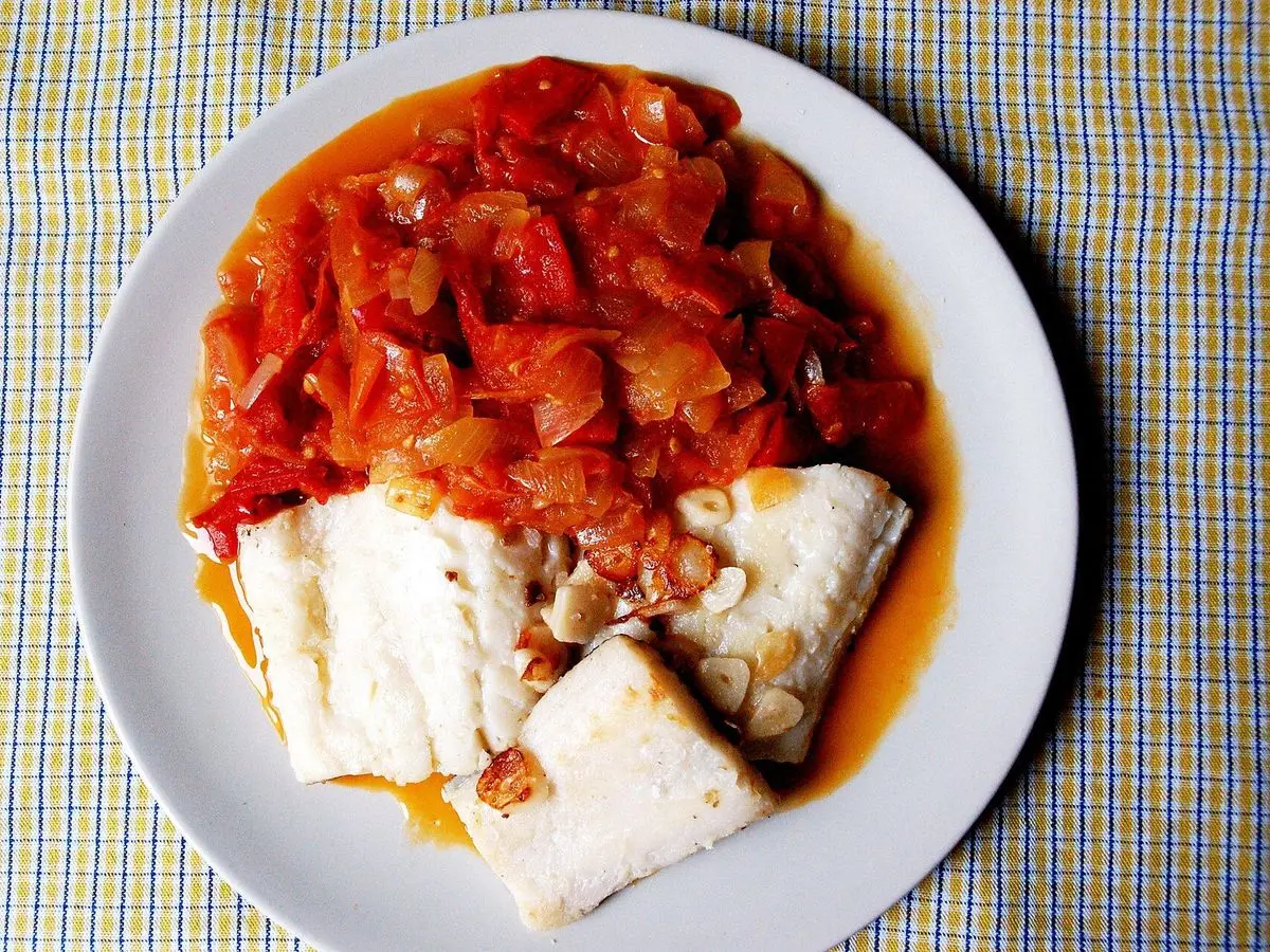 Plato de bacalao con pimiento rojo, tomate y cebolla guisados, sobre un mantel de cuadros