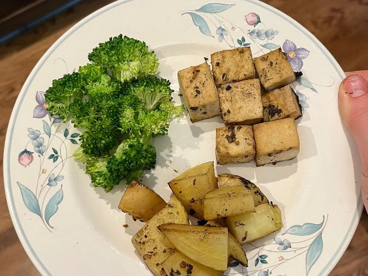 Plato con cubos de tofu al horno, brócoli y patatas troceadas sobre un plato de flores azules