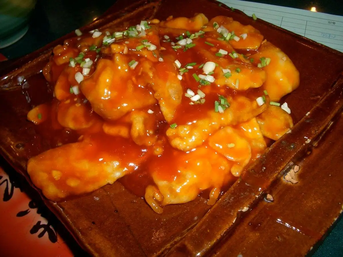Tofu crujiente bañado en salsa agridulce roja con cebollino picado sobre una bandeja de madera