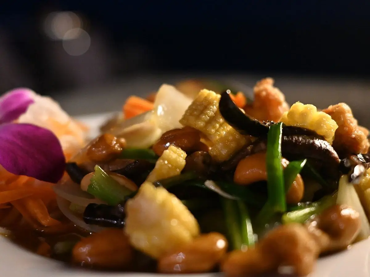 Salteado de verduras con anacardos, judías verdes y maíz tierno servido en un plato blanco