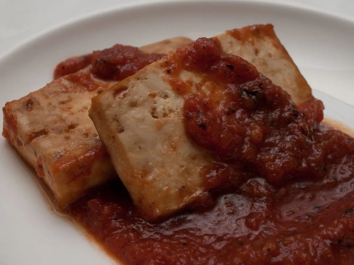 Lonchas de tofu al horno cubiertas de salsa barbacoa roja sobre un plato blanco