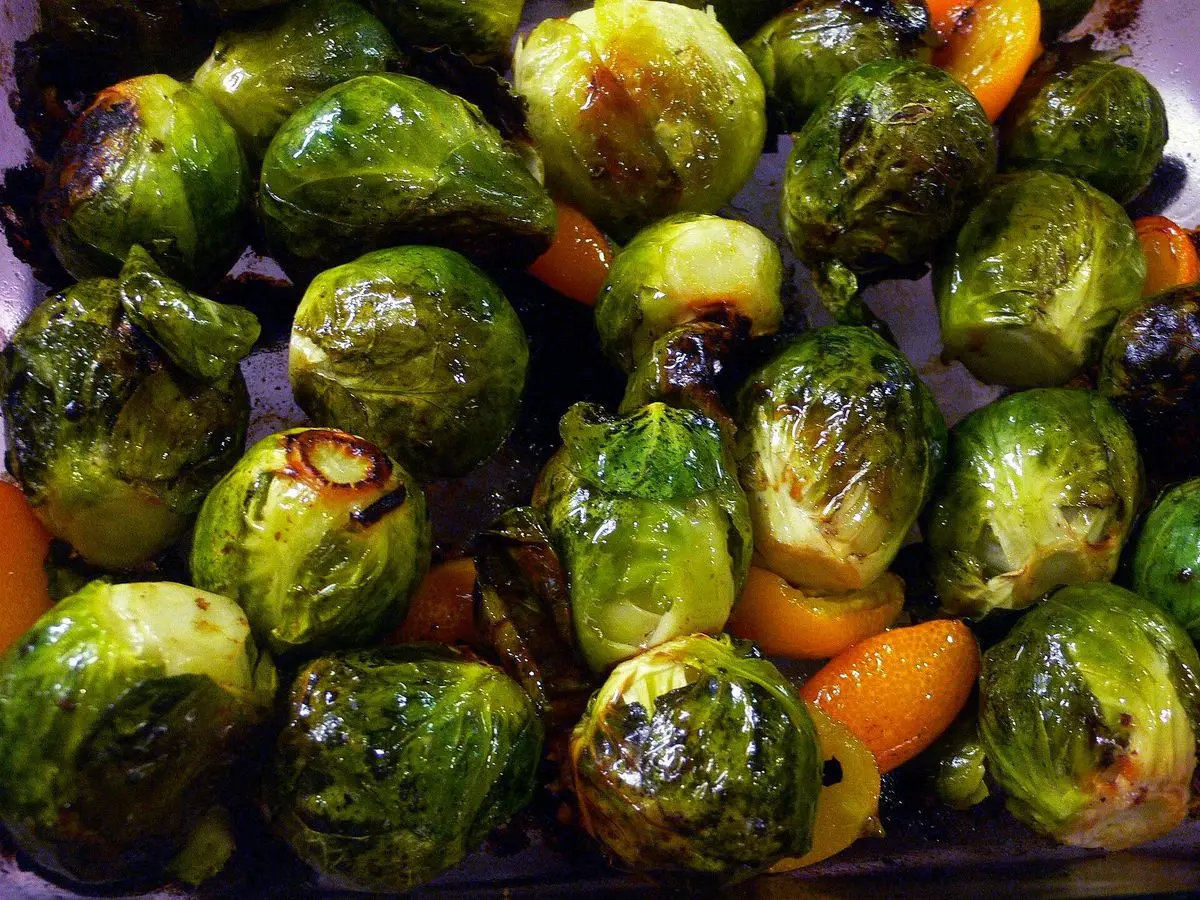 Coles de Bruselas asadas y doradas con trozos de naranja en una fuente