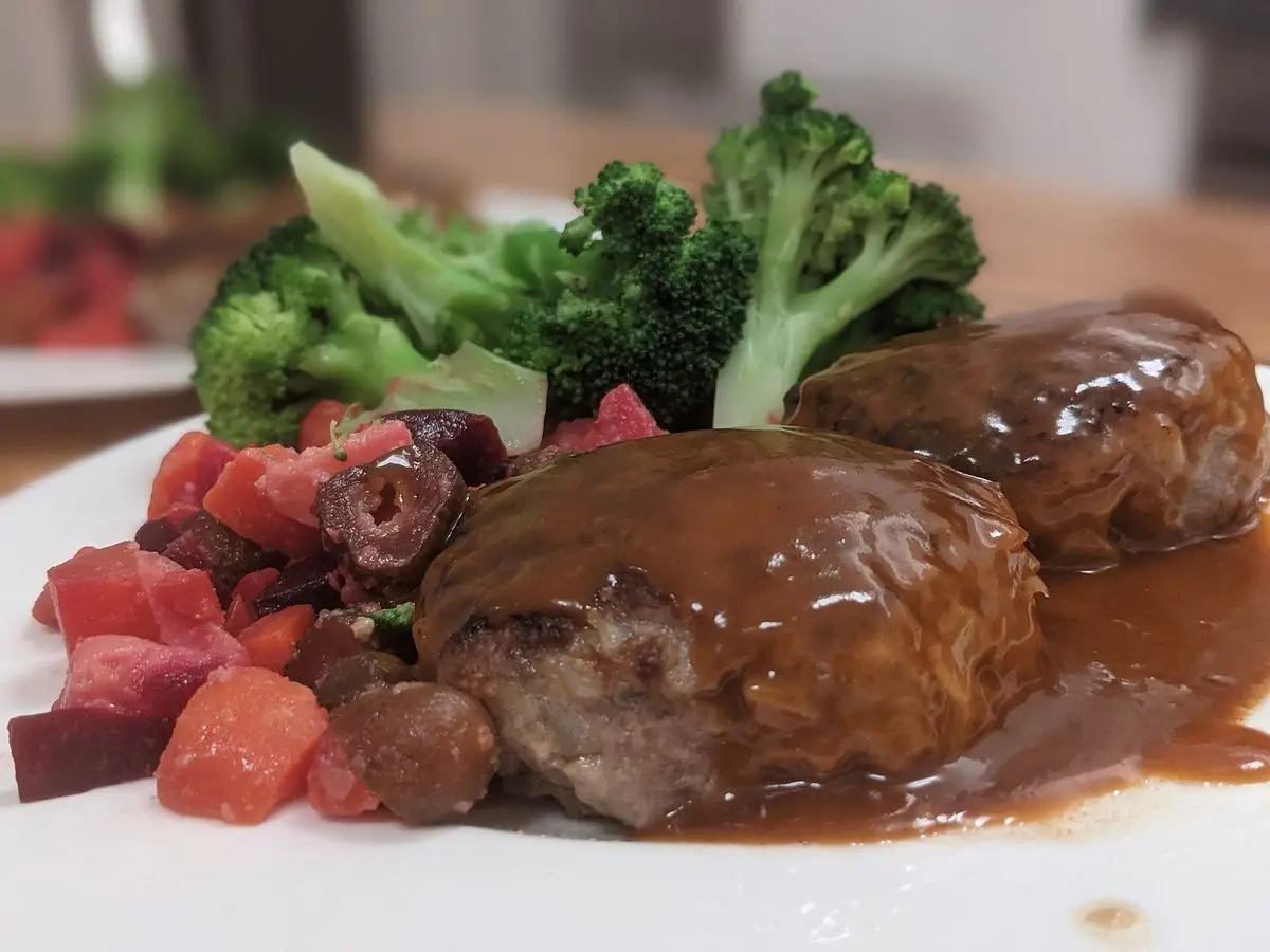 Dos hamburguesas japonesas con salsa oscura, brócoli y verduras en un plato blanco