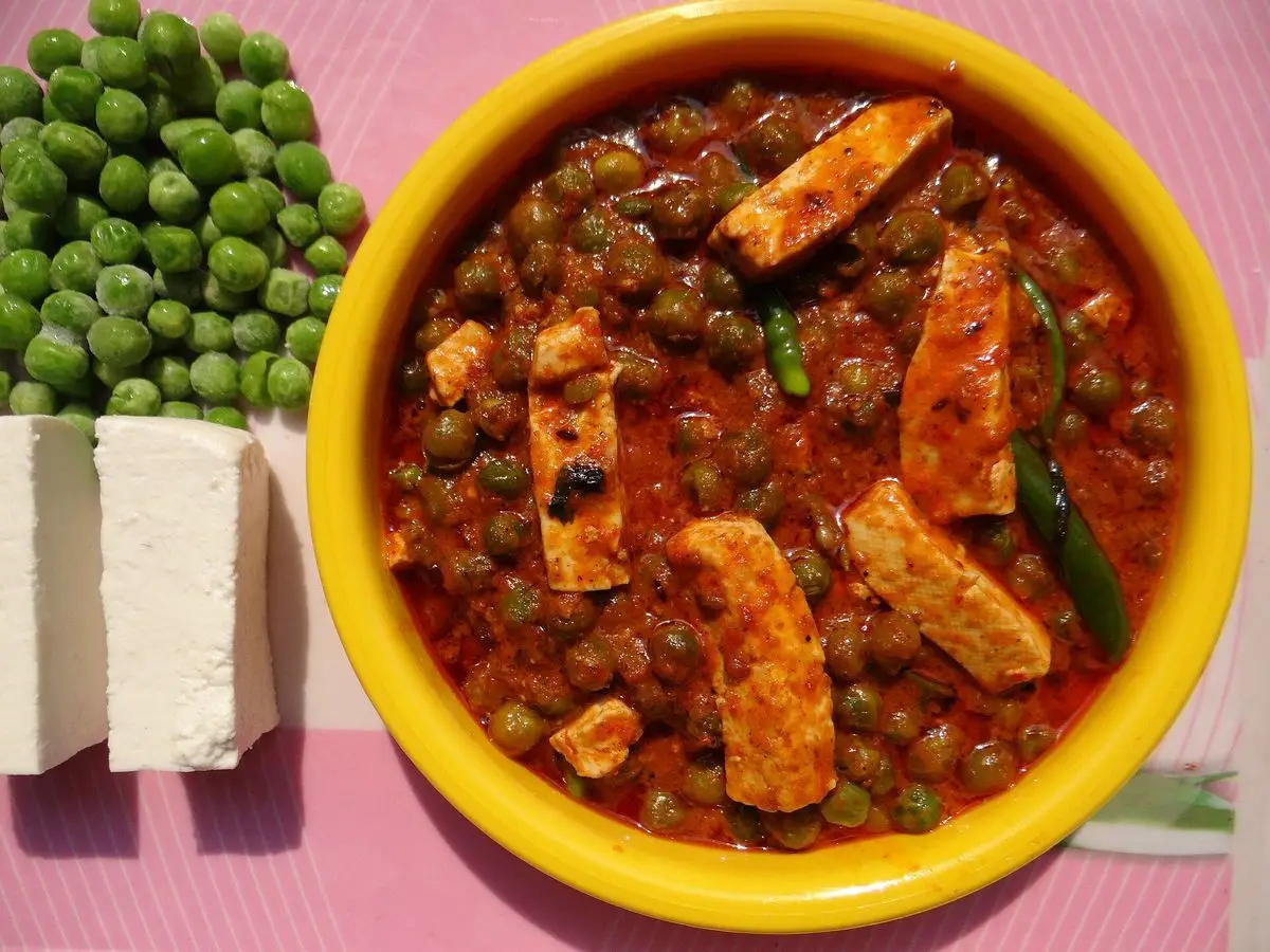 Cuenco amarillo de curry rojo con guisantes y dados de queso blanco o tofu