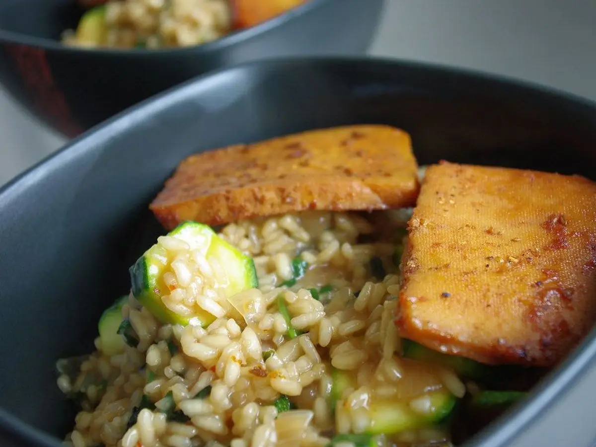 Cuenco con filetes de tofu horneado dorado sobre arroz con calabacín