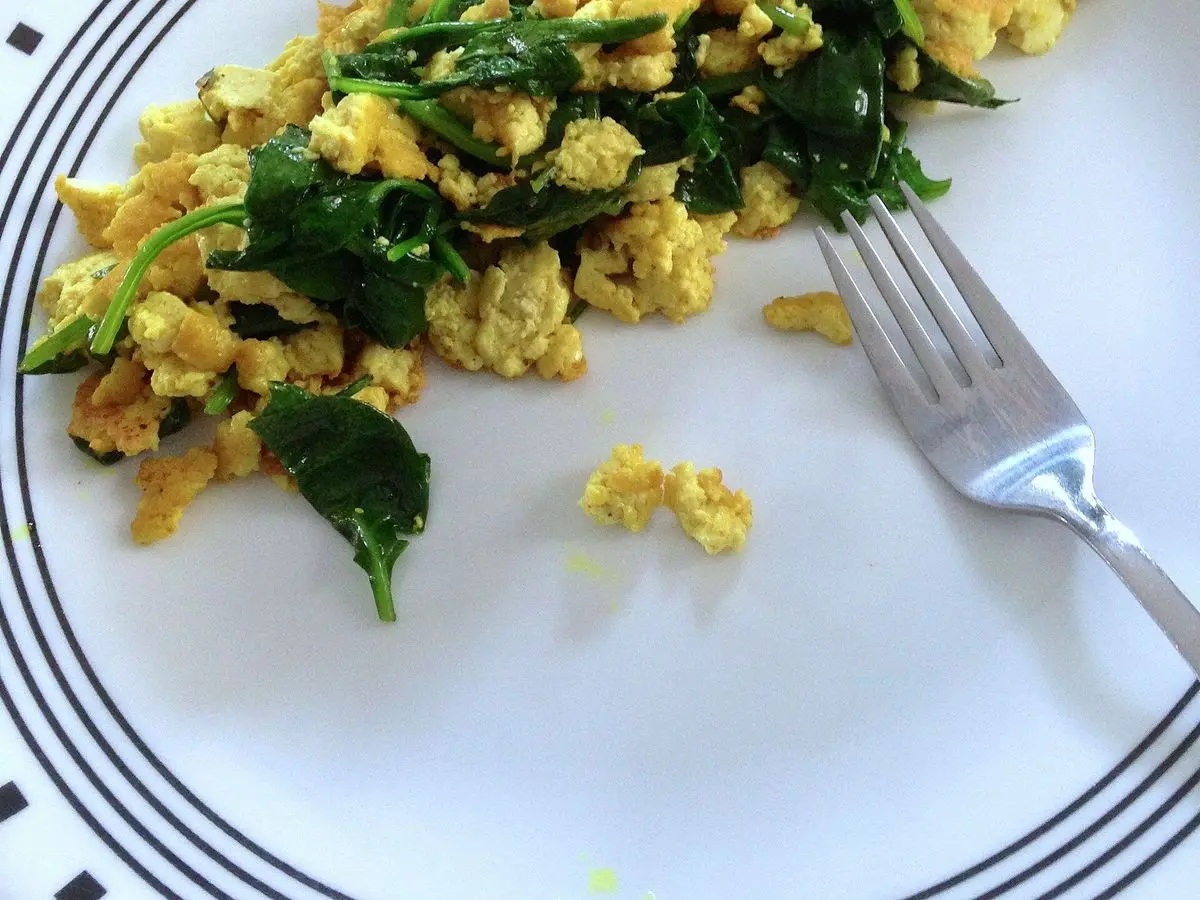 Plato de tofu revuelto amarillo con hojas de kale verdes y un tenedor