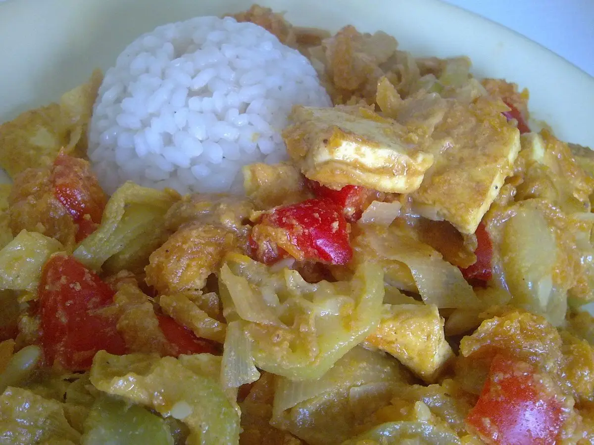 Plato de verduras con tofu en salsa amarilla acompañado de una bola de arroz blanco