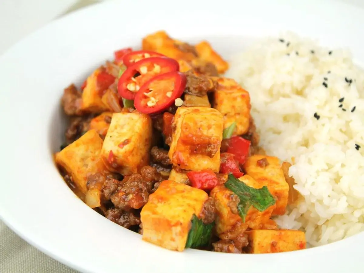 Tofu en dados con salsa roja y guindilla junto a arroz blanco en un plato
