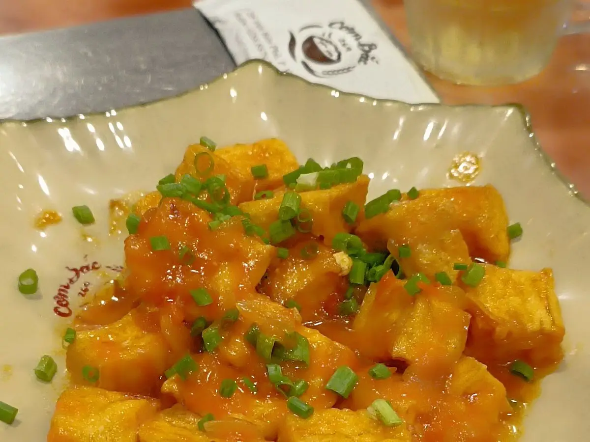Cubos de tofu dorado en salsa anaranjada de tomate con cebolleta picada en un plato